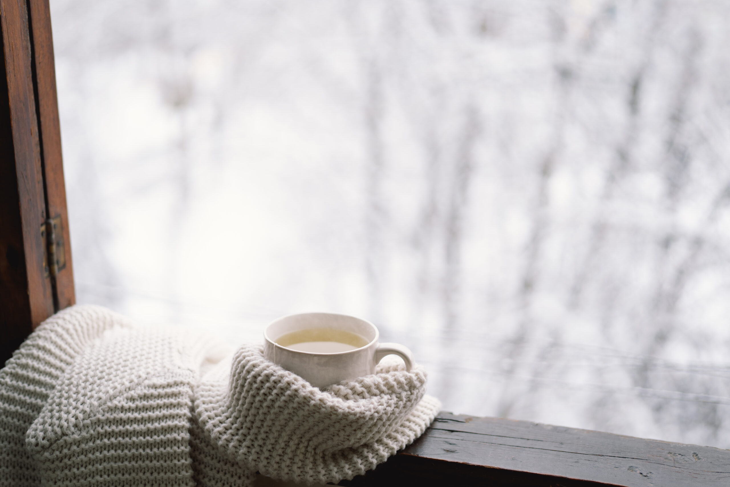 Cozy winter still life. Cup of hot tea with a warm sweater on a vintage wooden windowsill. Cozy home concept. Sweet home.