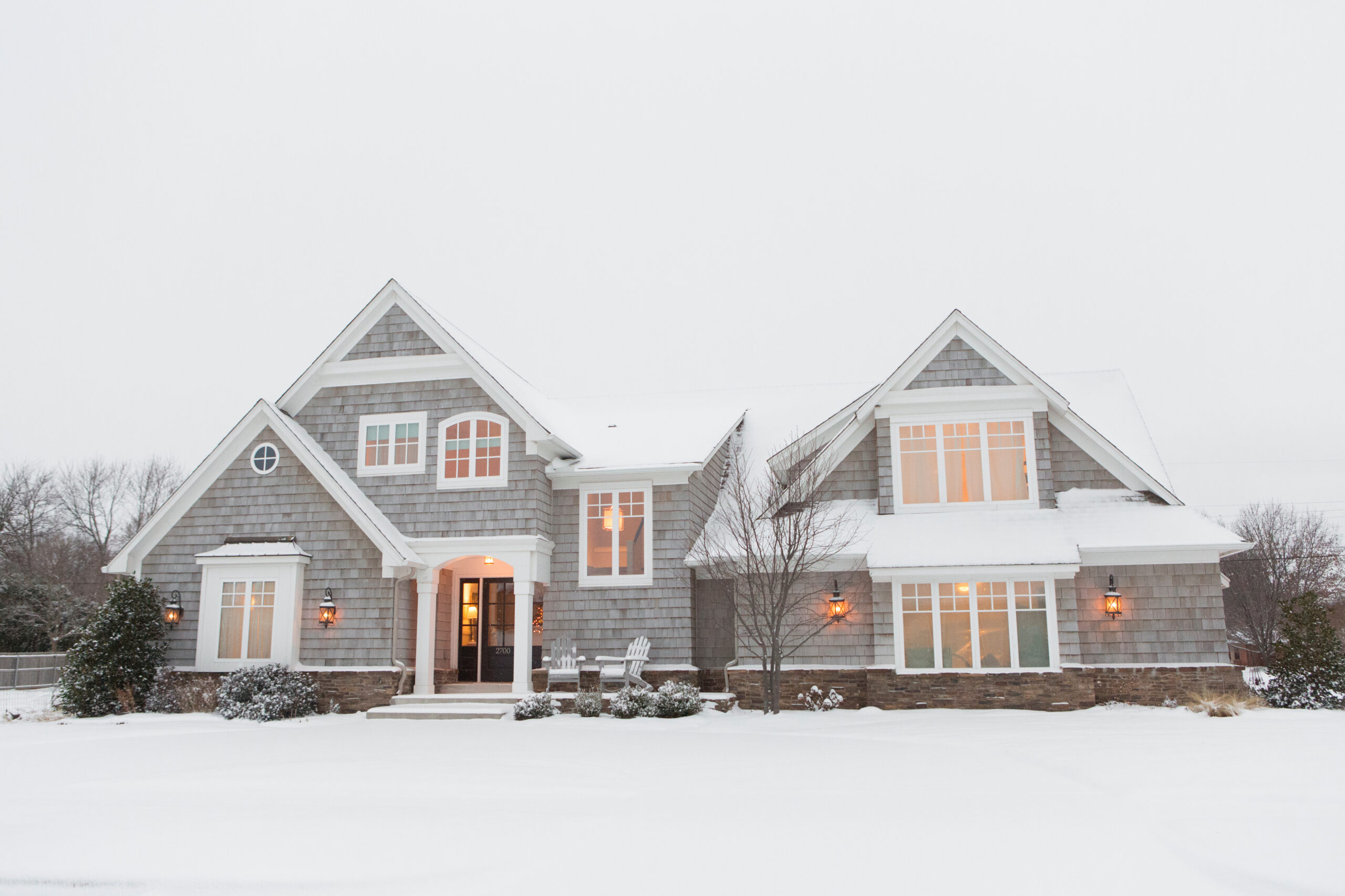 Wood shingled home in snow with warm lights illuminating windows